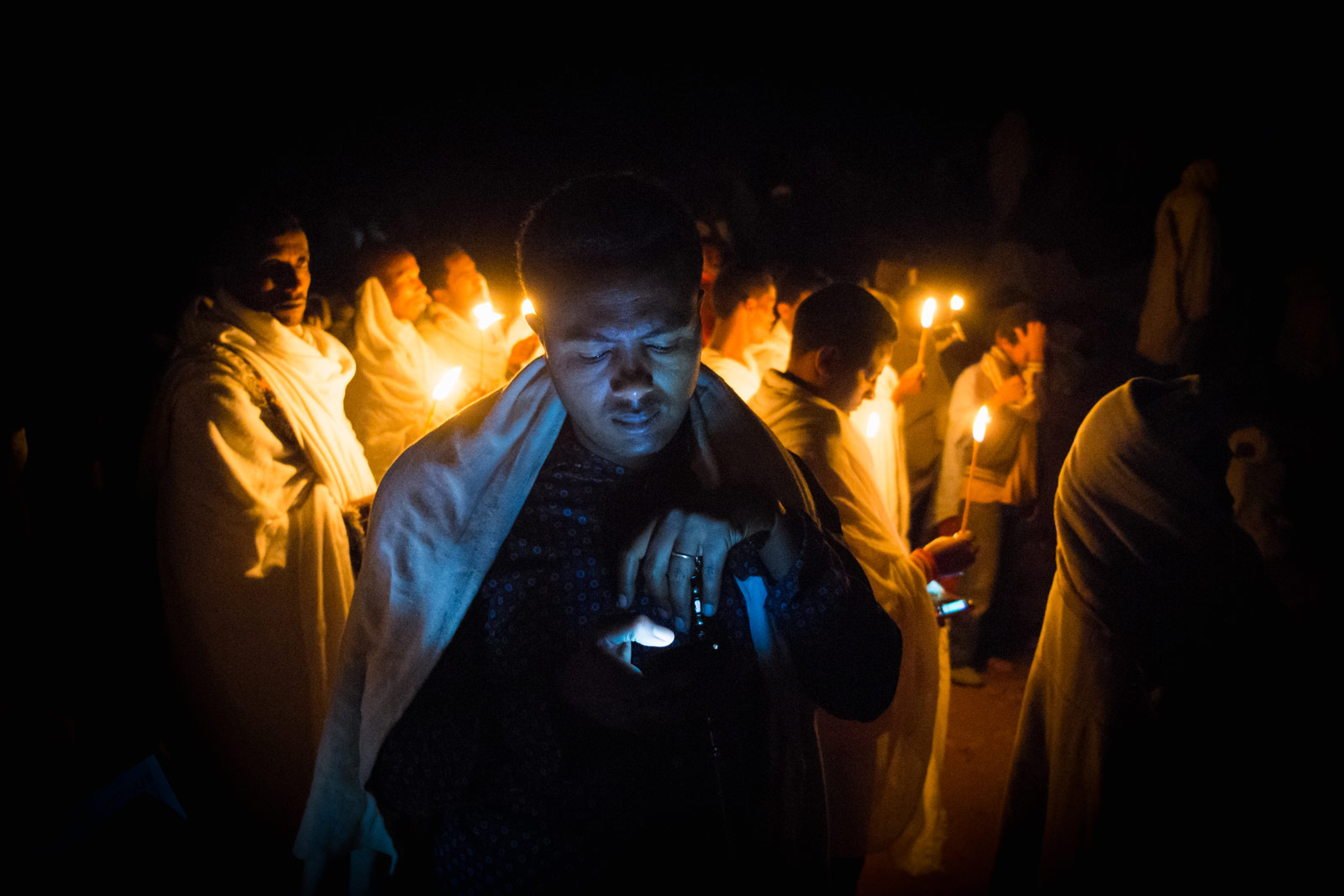 Surrounded by candlelight, a pilgrim is lit by the light of his phone in Lalibela, Ethiopia