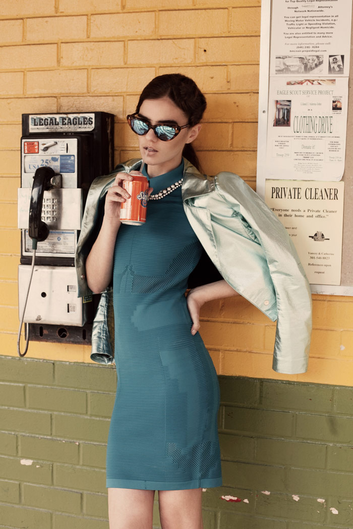 young woman with sunglasses sipping on a soda next to a payphone