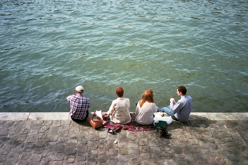 four people sitting on the edge of the Seine river